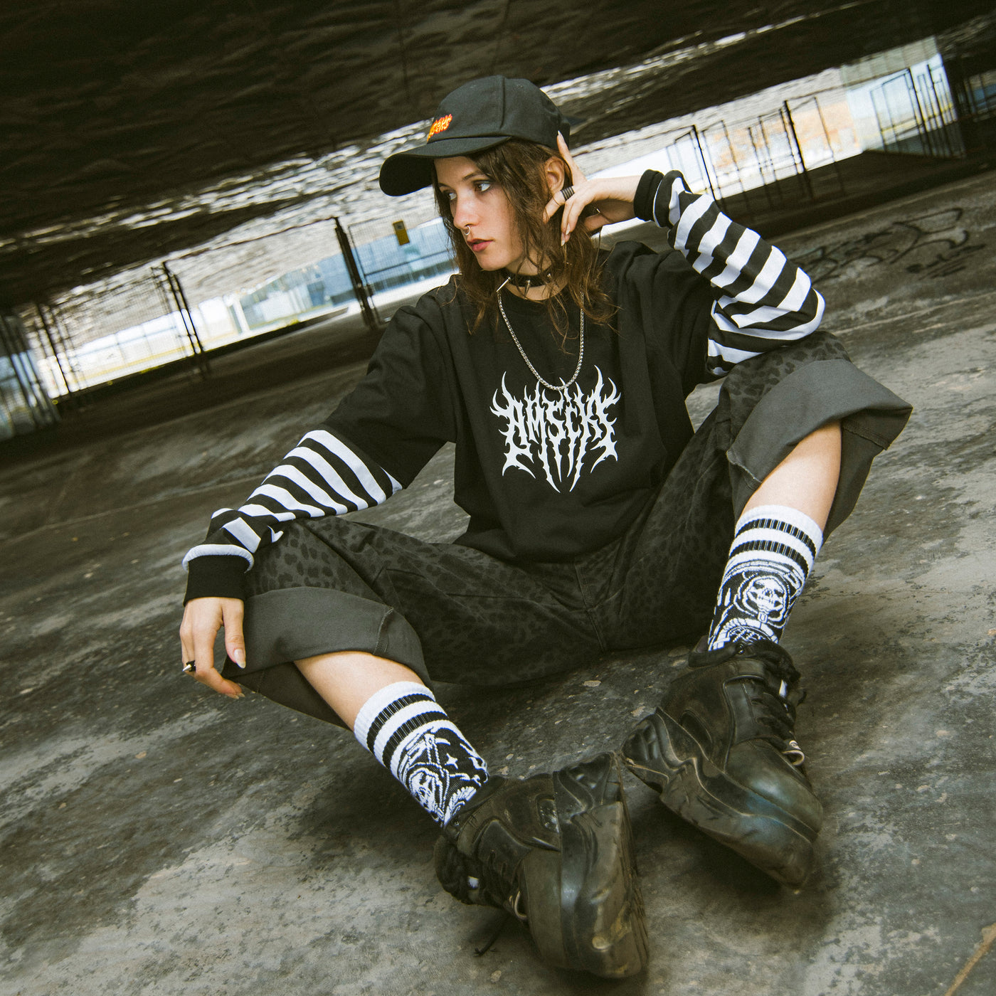 Woman wearing black alternative streetwear outfit with striped sleeves and grim reaper socks sitting casually american socks