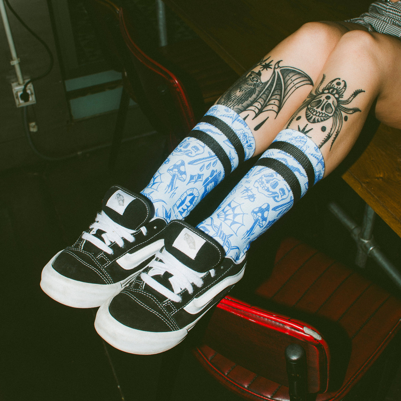 Blue socks with tattoo like illustrations worn by a woman with legs resting on chair american socks
